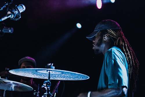 person man playing drums beside man wearing gray fitted cap drummer