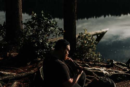 person man playing guitar near trees and and body of water nature