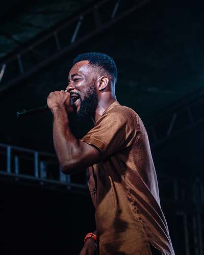 person man singing on stage white wearing brown crew-neck shirt people