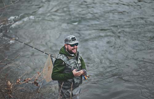 person man smiling holding black fishing rod near body of water people