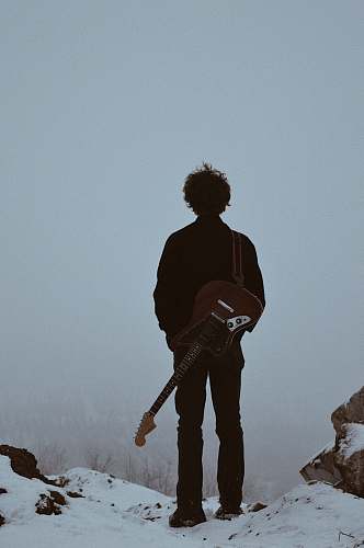 person man with guitar on his back standing on cliff people