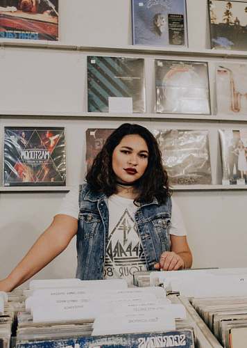 person woman in blue denim button-up vest stands near organized folders and music albums people