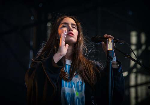 person woman performing on stage with closed eyes and holding a microphone people