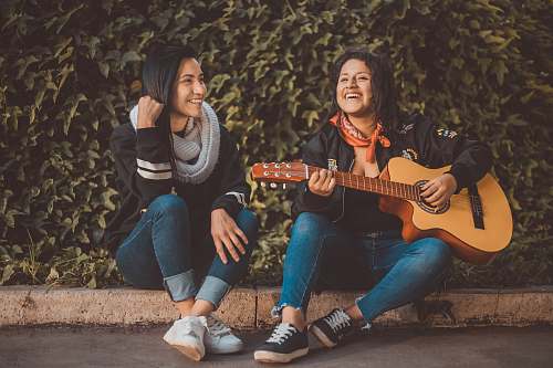 person woman playing guitar sitting beside with woman wearing scarf people
