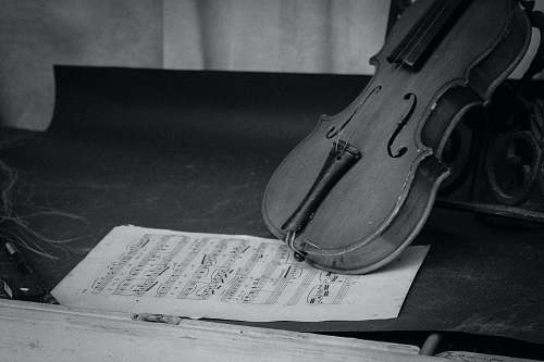 black-and-white grayscale photography of violin on table with music sheet grey