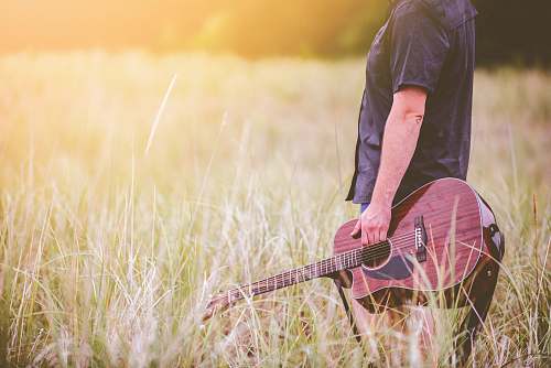 grass man carrying brown cutaway acoustic guitar standing on green grass field guitar player