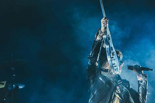 blue man holding electric guitar and microphone in front of lights inside dim room with smoke microphone