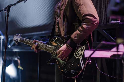 guitar man playing black electric guitar beside black microphone with stand person