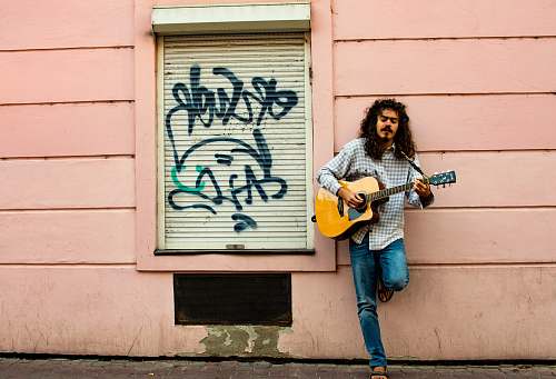 human man playing guitar on street during daytime people