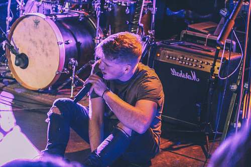 human vocalist man holding microphone sitting in front of Marshall guitar amplifier near drum kit person