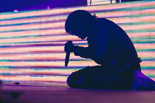 human silhouette photo of man sitting on stage while holding dynamic wireless microphone person