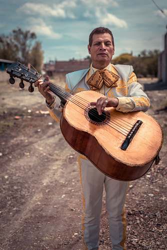 human standing man holding brown sting musical guitar during daytime person