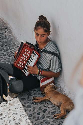 human woman playing accordion beside laying dog during daytime person