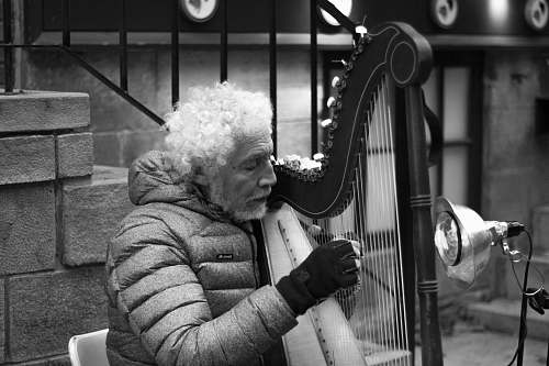 human grayscale photo of man playing harp near stairs black-and-white
