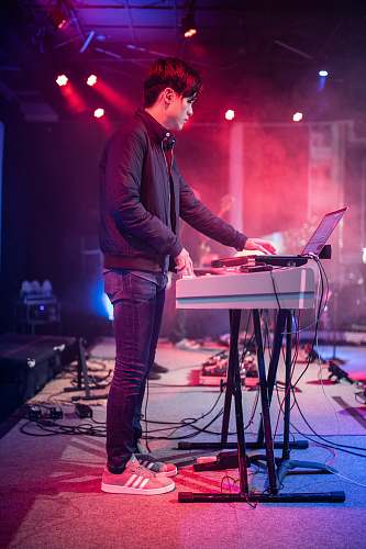 human man in black long sleeve shirt and blue denim jeans standing beside table musical instrument