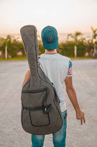 human man looking at green trees carrying grey guitar case people