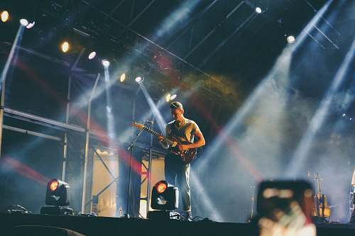 human man playing guitar on stage during nighttime people