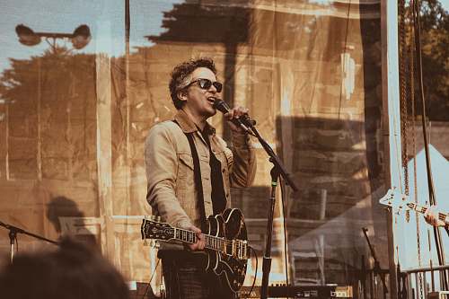 human man standing while holding black guitar and microphone people
