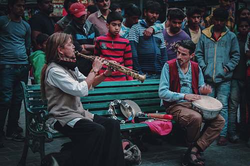 human people gathering looking at the man sitting on bench playing wind instrument people
