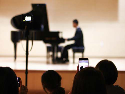 human person taking photo of person playing piano on stage people