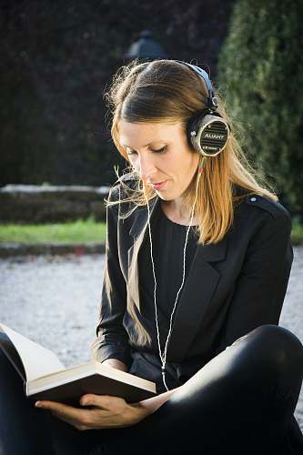 human selective focus photography of sitting woman wearing headphones while reading book sitting