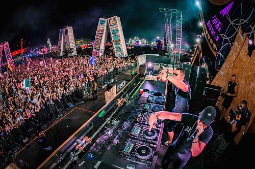 crowd two men playing DJ controllers at night time light