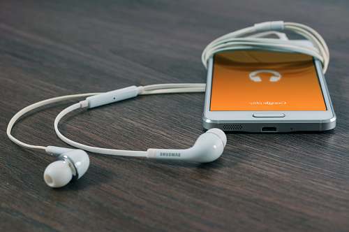 tech white Samsung Android smartphone turned beside white earbuds on brown board phone