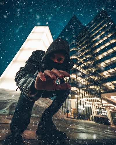 person close-up photography of man kneeling on ground front of gray high-rise building during snow weather human