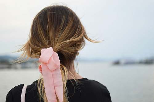 woman focus photography of woman with pink hair bow facing on body of water hair