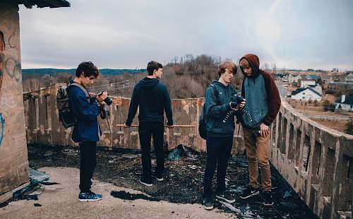 person four man wearing blue jackets standing beside house looking at their cameras during daytime human
