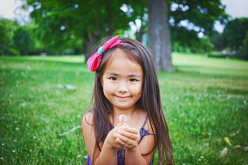 human girl wearing black top while standing and holding flower on green grass girl
