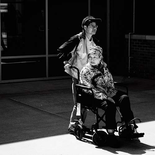 black-and-white gray scale photo of man pushing wheelchair wheelchair