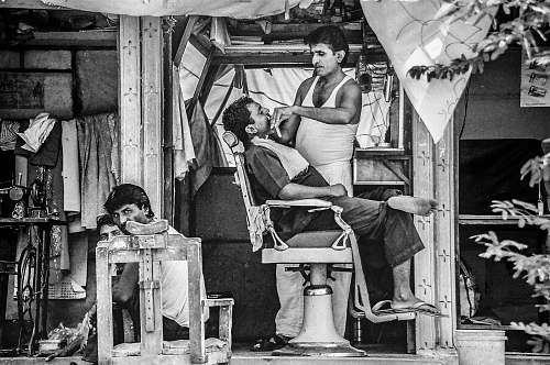 human grayscale photo of barber trimming man's beard black-and-white