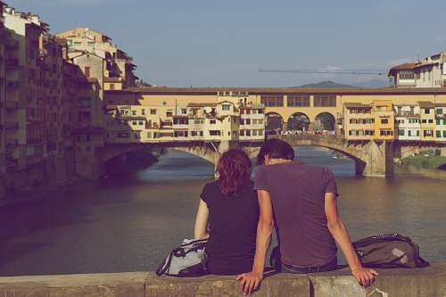 person man and woman sitting together in front of body of water during daytime human