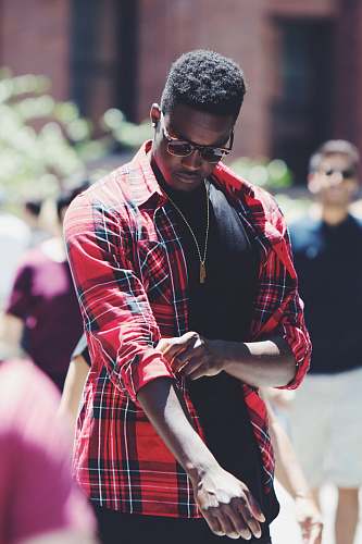 human man fixing his red, black, and white plaid sport shirt sleeve during daytime person