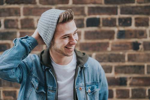 person man holding the back of his head while smiling near brick wall human