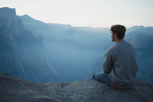 person man in gray shirt sits on cliff blue