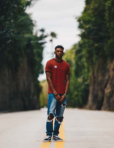 person man in red shirt and blue distress denim jeans standing in middle of road human