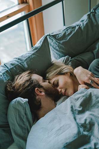 human man kissing woman's forehead while lying on bed couple