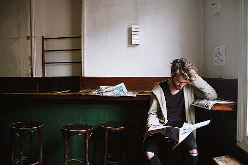 person man sitting on bar stool while holding newspaper bar stool