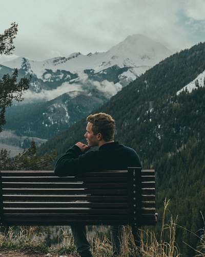 person man sitting on bench on top of the mountain trees
