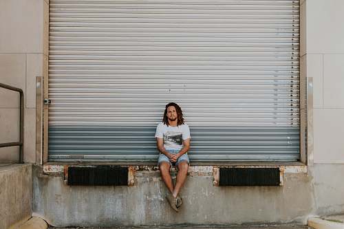 person man sitting on pavement in front of roller shutter human