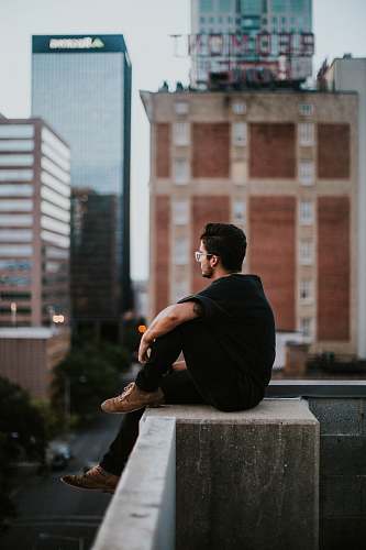 person man sitting on white concrete building during daytime human