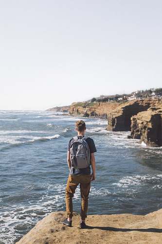 person man standing on cliff looking at body of water beach