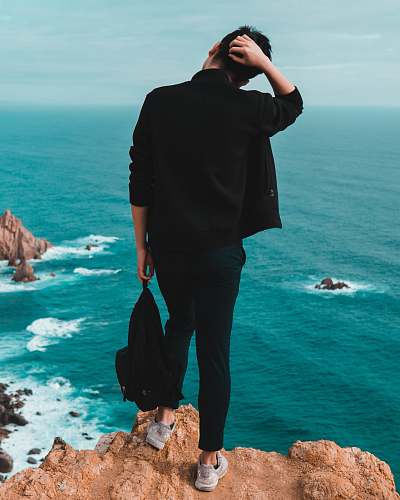 person man standing on top of mountain facing backwards at body of water human