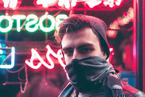 person man with face half covered with mask standing in front of red and green neon light signage during daytime human