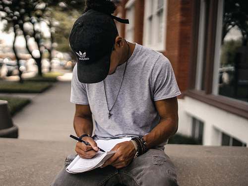 human person in black adidas cap sitting on bench writing on notebook person