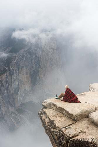 person person sitting on cliff under cumulus cloud human