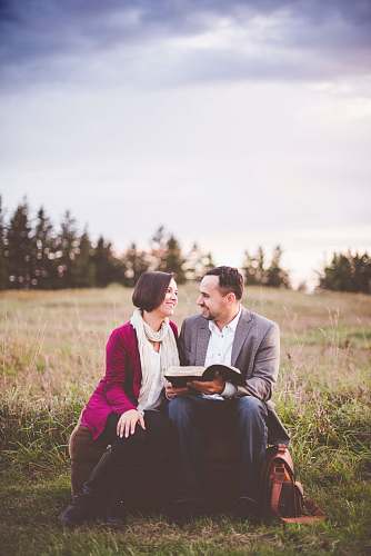 person photo of man reading book to woman under grey cloudy sky couple