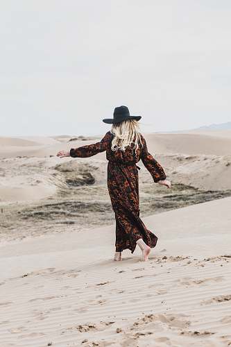 person photo of person wearing brown and orange floral maxi dress walking barefooted along deserted land woman